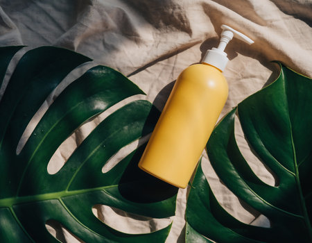 A yellow lotion bottle is placed on a monstera leaf and beige fabric, creating a natural and minimalist aesthetic.の素材
