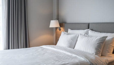 A well-lit hotel room featuring a comfortable bed with white linens and pillows, creating a welcoming and relaxing atmosphere for guests.の素材
