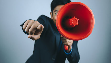 A man in a suit uses a red megaphone, pointing directly at the viewer, symbolizing focused communication and a powerful announcement.の素材