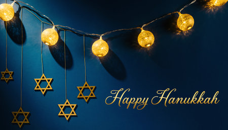 A festive Hanukkah scene featuring Star of David decorations hanging beneath a string of warm, glowing lights against a deep blue background.の素材