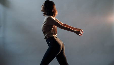 A woman with short hair is captured in motion in a studio setting, her arms outstretched, creating a dynamic and engaging image.の素材