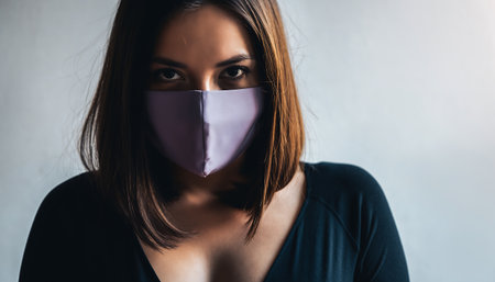 A woman wearing a protective face mask looks directly at the camera with a focused expression, emphasizing personal safety.の素材