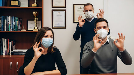 Man and woman in medical masks showing ok sign with fingers in officeの素材