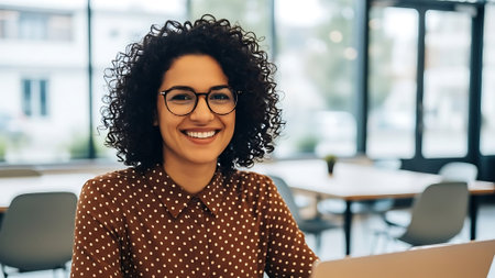 smiling african american businesswoman in eyeglasses using laptop in officeの素材