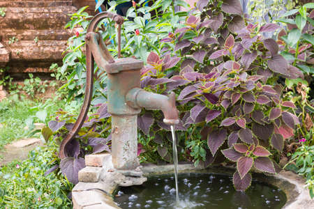 An old fashioned hand water pump above old water well, with plantsの写真素材