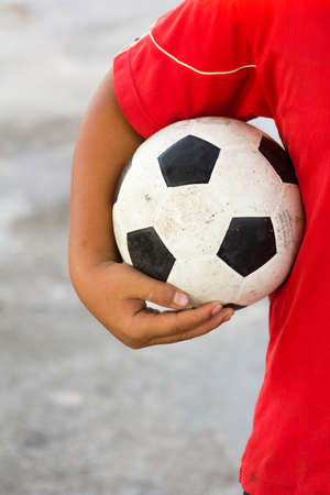 boy with red t-shirt holding dirty black white football or soccer sport ball in handの写真素材