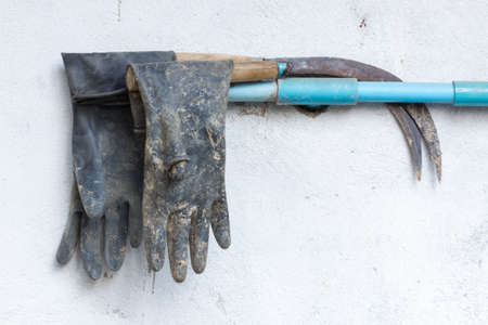 dirty rusty sickle and dirty rubber gloves hanging on wallの写真素材