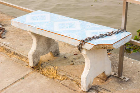 broken white rock bench locked to prevent stealing, public park in thailand