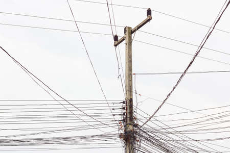 electric post with messy wires on white skyの写真素材
