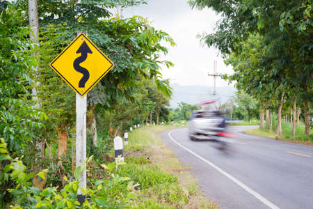 Winding road sign in the forest with blurred car and motorcycle.の写真素材