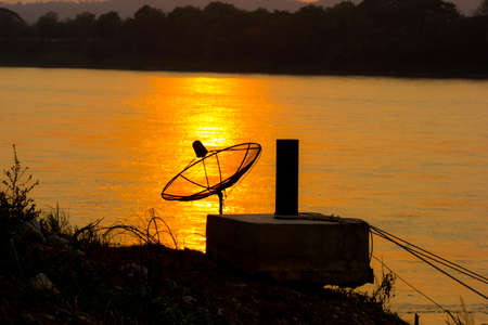 Satellite dish on the reflection on the river in sunset background.