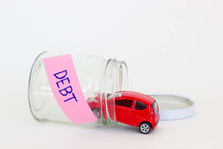 horizontal photo of red car toy going into the glass bottle with the word DEBT on its pink label.の写真素材