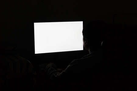 Back view of a man working in front of blank computer screen in dark room, copyspace. computer addiction concept.の写真素材