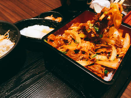 Japanese traditional dish Gyudon made from thinly sliced beef, onion, soy sauce on rice with soup. Dark tone. using chopstick.の写真素材