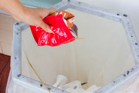 closeup hand throws away red waste material into trash container.の写真素材