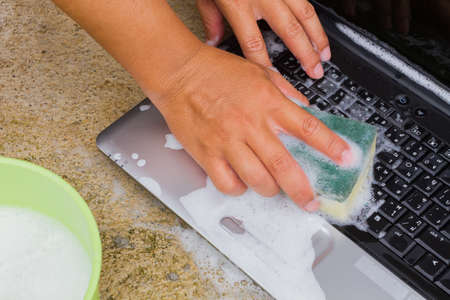 closeup cleaning computer notebook with dish washing soap, technology concept