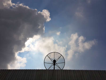 Silhouette of satellite dish on roof with cloudy skyの写真素材