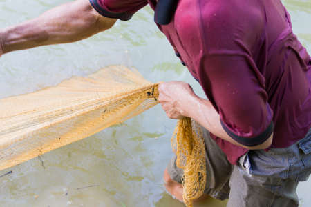 close-up asian fisherman in dark red polo shirt pulling the net out of the pond, focusing on the handの写真素材