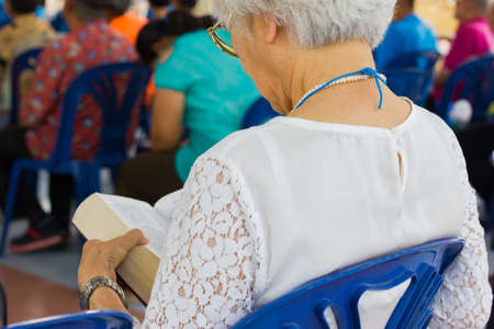 old woman with white hair reading holy bible in a churchの写真素材