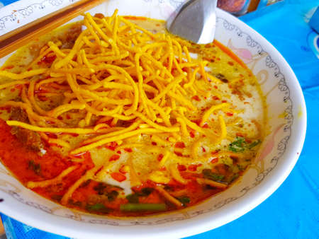 Khao Soi , Northern Thai Style Curried Noodle Soup with chopsticks and spoon on blue tableの写真素材
