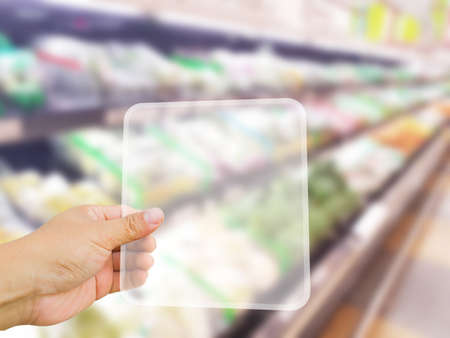 asian left hand holding blank digital transparent tablet on the background of blur supermarket interiorの写真素材