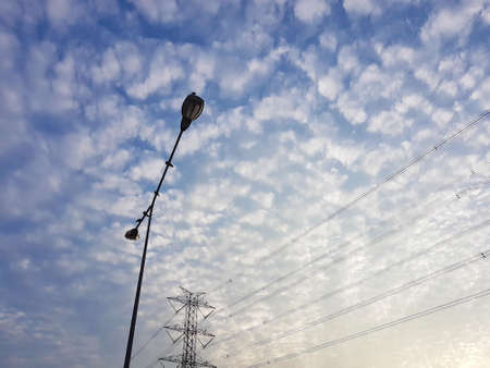 High voltage post with street light under cloudy blue sky backgroundの写真素材