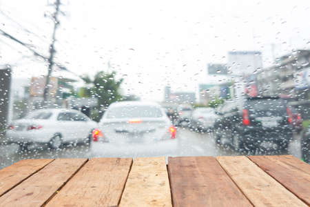retro old wooden board empty table in front of blurred raining on the windshield of a vehicle on the streetの写真素材