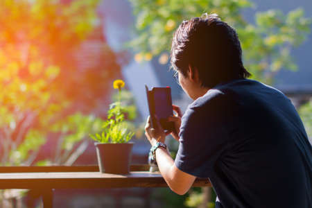 Asian man using smartphone shooting marigold flower on wooden table. Copyspace.の写真素材