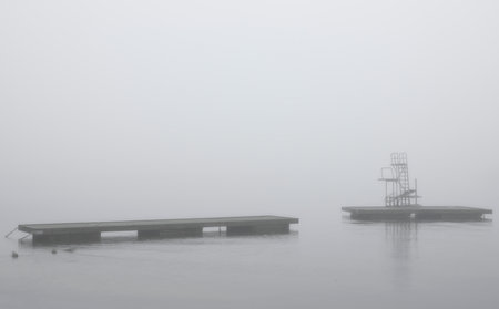 Swim platform floating on a calm lake on a foggy morningの写真素材