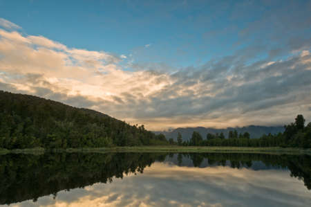 Sunrise above a lake on a wind still morning and the sky reflects in the lakeの写真素材
