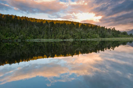 Sunrise above a lake on a wind still morning and the sky reflects in the lakeの写真素材