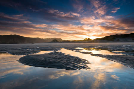 Sunrise above beach with reflection on incoming tideの写真素材
