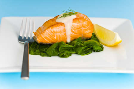 Salmon steak on spinach, decorated with lemon, sauce and forkの写真素材