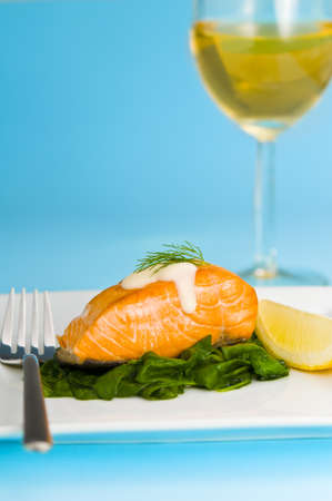 Salmon steak on spinach, decorated with lemon, sauce and forkの写真素材