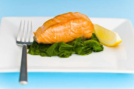 Salmon steak on spinach, decorated with lemon and forkの写真素材