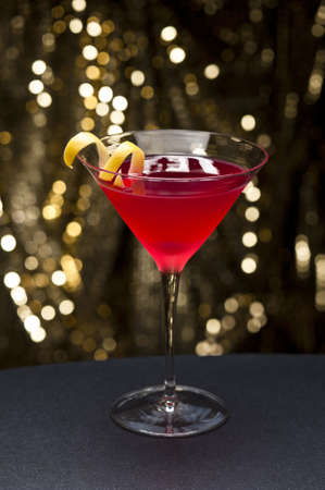 Cosmopolitan cocktail with lemon garnish in front of a gold glitter backgroundの写真素材