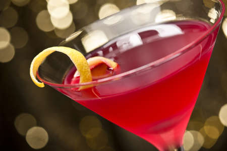 Cosmopolitan cocktail with lemon garnish in front of a gold glitter backgroundの写真素材