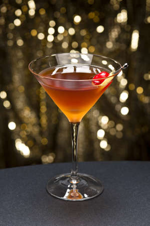 Manhattan cocktail garnished with a cherry and lemon and gold glitter back groundの写真素材