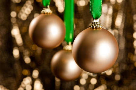 Three golden Christmas baubles in front of a gold glitter background for Christmas or decorationの写真素材