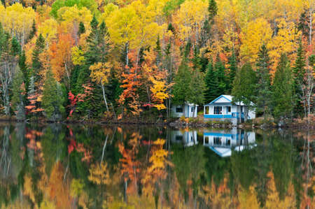 Beautiful reflections of a autumn forest and a house in a lakeのeditorial素材