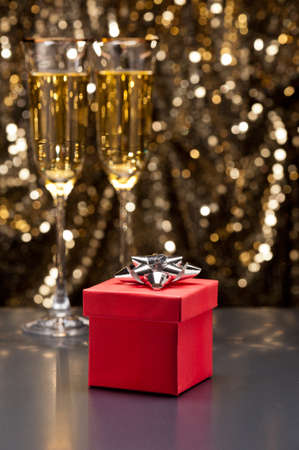Champagne glasses and gift in front of gold glitter backgroundの写真素材