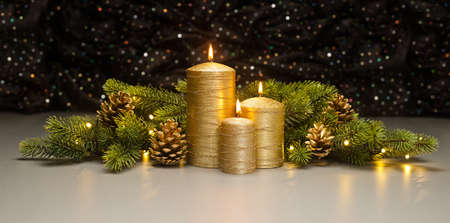 Three golden Candles with Christmas tree branches and pine cones decoratedの写真素材