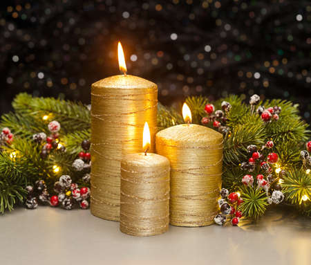 Three golden Candles with Christmas tree branches and red berries decoratedの写真素材