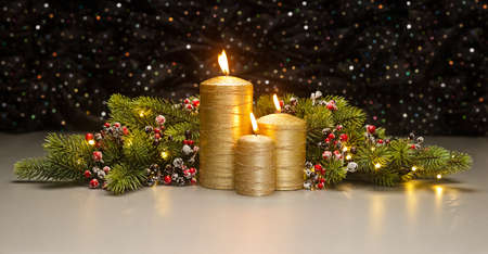 Three golden Candles with Christmas tree branches and red berries decoratedの写真素材
