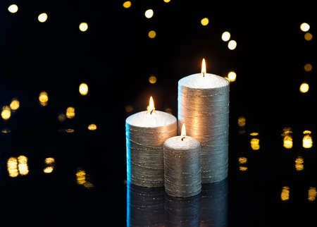 Three silver candles in front of dark background