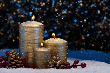 Three Golden Candles in snow with snowfallの写真素材