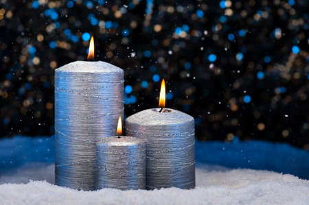 Three Silver Candles in snow with snowfallの写真素材
