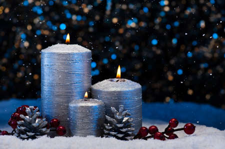 Three Silver Candles in snow with snowfallの写真素材