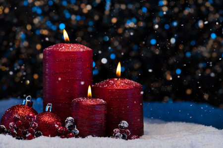 Three Red Candles in snow with snowfallの写真素材