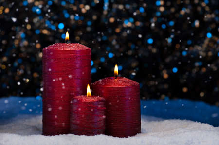 Three Red Candles in snow with snowfallの写真素材